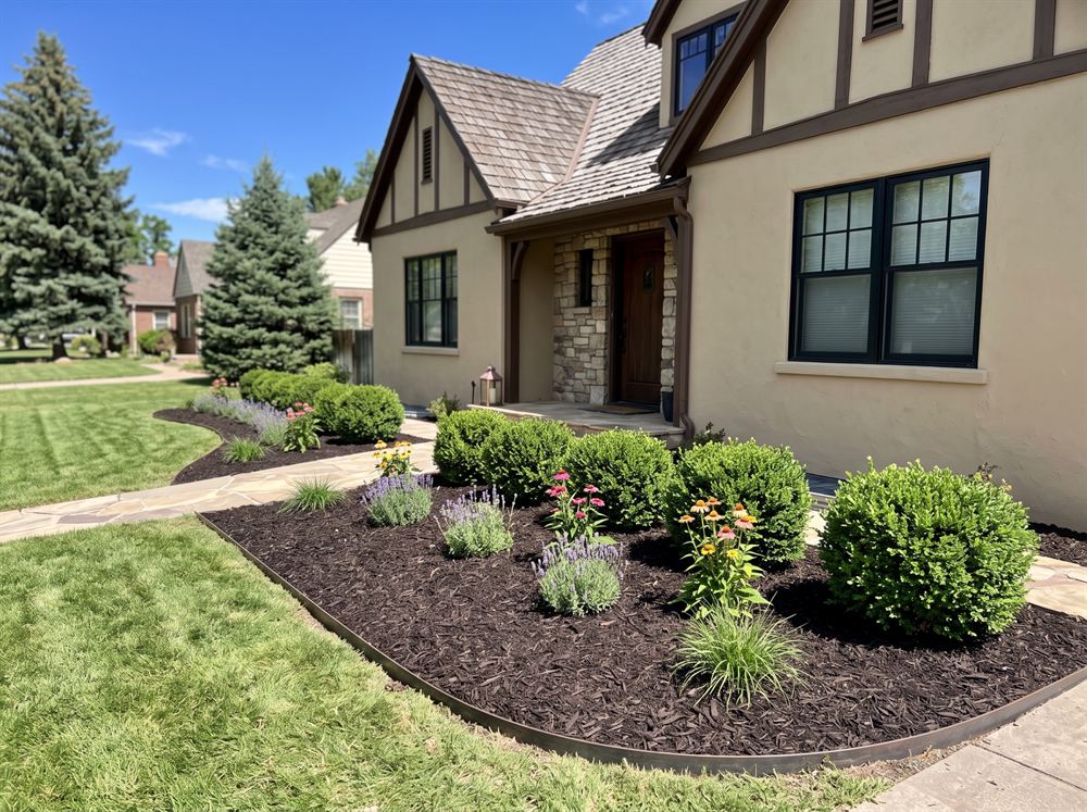 A freshly mulched garden bed with trimmed shrubs beside a house